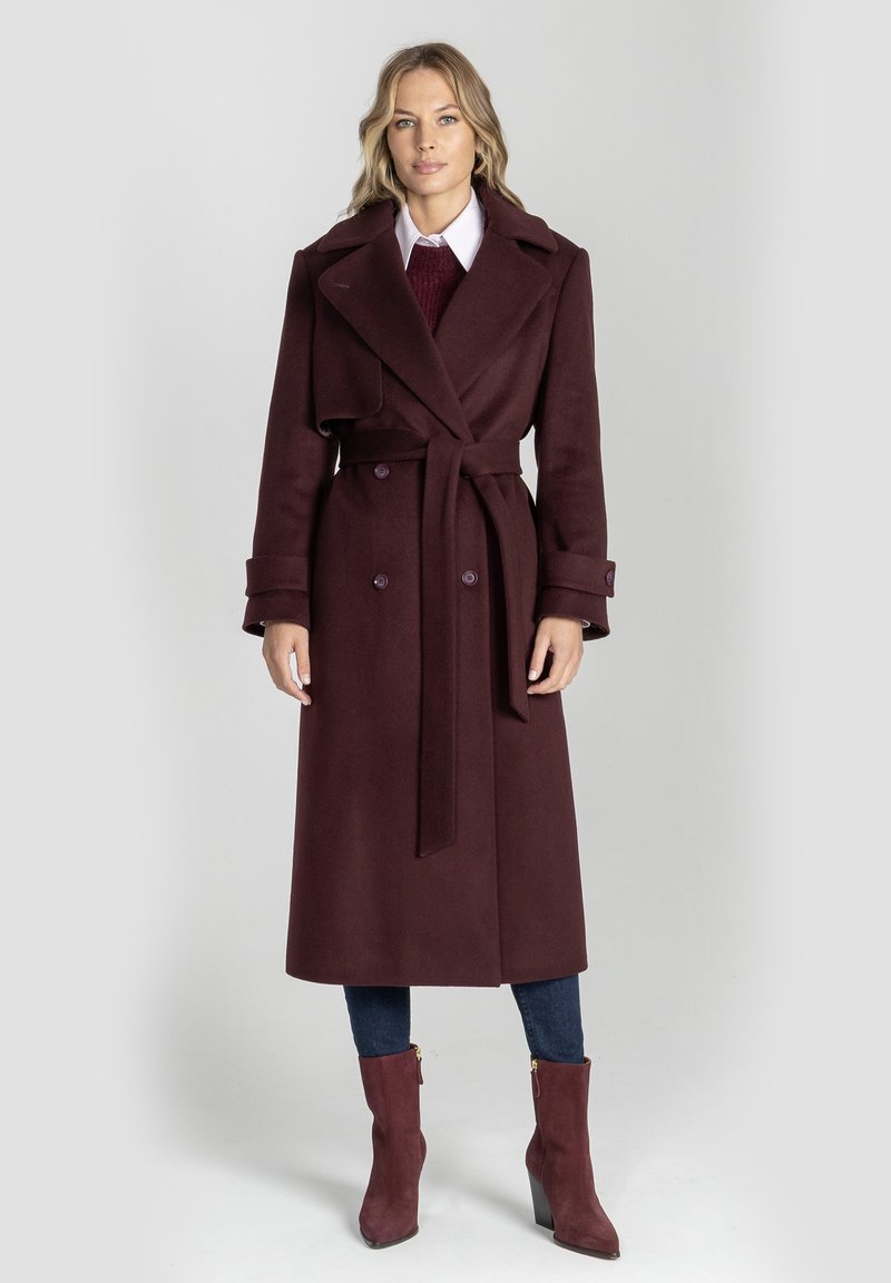 Bordowy długi płaszcz z podwójnym zapięciem, szerokimi klapami i wiązaniem w talii. Miękka tkanina o gładkiej fakturze, zestawiona z dopasowanymi dżinsami i botkami za kostkę.