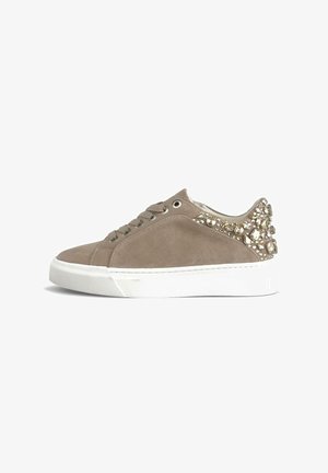 Sneaker in suede beige con suola in gomma bianca, caratterizzata da borchie metalliche decorative sul tallone e lacci tondi. Texture complessivamente liscia.