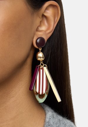 Ucho ozdobione wielokolorową, zwisającą kolczykiem z ciemnym, okrągłym sztyftem, złotą kulką oraz paskowanymi i jednolitymi geometrycznymi kształtami w bordowym, kremowym i zielonym kolorze.