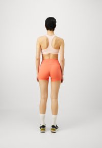 Soutien-gorge de sport rose clair avec un design dos nageur, associé à des shorts orange vif. Les shorts ont une taille haute et une texture lisse.