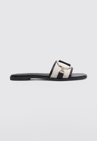 Sandalia deslizante en negro y crema con parte superior tejida texturizada, suela plana y un acento de hardware dorado en la correa.