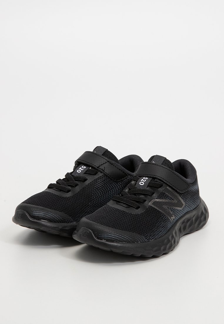 Une paire de baskets New Balance 520 noires avec des tiges en mesh, des bandes Velcro et des semelles texturées rembourrées sur une surface gris clair.