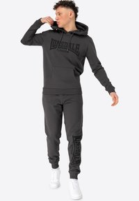Grå bomulds-hættetrøje med et stort sort Lonsdale-logo og frontlomme, parret med matchende grå joggers med logo-detaljer og hvide sneakers.