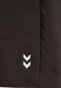 Czarny materiał o gładkiej fakturze z naszytą kieszenią i trzema białymi akcentami w kształcie szewronu w pobliżu dolnego prawego rogu.