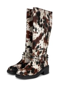 Botas de vaquero altas con un patrón de piel de vaca en negro, marrón y blanco, y una correa de cuero con tachuelas alrededor del tobillo sobre tacones cuadrados negros.