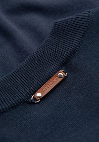 Pull bleu marine avec un col côtelé, présentant une étiquette en cuir avec un texte en relief, fixée par une quincaillerie de couleur argentée. Texture douce.