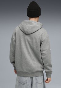 Grå fleece sweatshirt med hætte og ribbet manchetter, der har en afslappet pasform og design på ryggen. Sammen med lyse denimbukser.