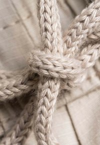 Cordón de fibra natural trenzado en un suave color beige, atado en un nudo, mostrando textura y detalle sobre un fondo beige claro.