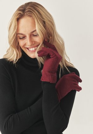 Burgundy ullhandskar med mjuk textur, med en åtsittande design och förstärkta handledsmuddar. Bärs av en person i en svart polotröja.