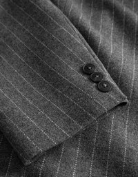 Γκρι μάλλινο σακάκι με μανίκι και λευκές ρίγες. Διαθέτει τρία μαύρα κουμπιά και μια απαλή, υφασμάτινη υφή.