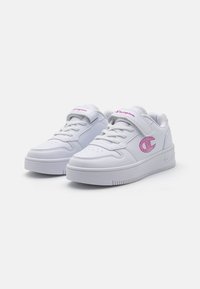 Baskets de sport blanches avec une tige en synthétique lisse, un détail de logo rose, un bout arrondi, un laçage plat et une semelle en caoutchouc texturé.