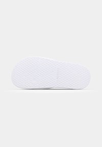 Semelle de chaussure en caoutchouc blanc avec de petites textures circulaires et une base lisse ; présente "LACOSTE" embossé pour le branding.
