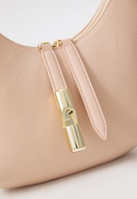 Borsa a tracolla in pelle rosa con una texture liscia, caratterizzata da una zip dorata e un accento metallico sulla linguetta della zip. Forma curvata e grana sottile.