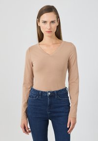 Maglietta beige a maniche lunghe con scollatura a V realizzata in un tessuto morbido, abbinata a jeans a vita alta blu scuro con chiusura a bottone e tasche frontali.