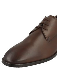 Hnědé kožené šněrovací boty s kulatou špičkou, hladkým povrchem, minimálním prošíváním a černou gumovou podrážkou.