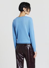 Helles blaues Sweatshirt aus weichem Material, mit Rundhalsausschnitt und langen Ärmeln, kombiniert mit glänzenden, dunkelbraunen hochgeschnittenen Hosen.