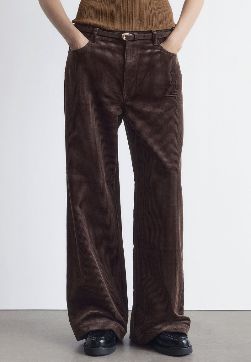 Brown corduroy wide-leg trousers with a textured finish, featuring front pockets and a black belt with a gold buckle.