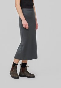 Jupe midi grise avec une taille élastique, assortie à des bottines brunes avec un panneau élastique sur le côté et une languette de tirage au talon.