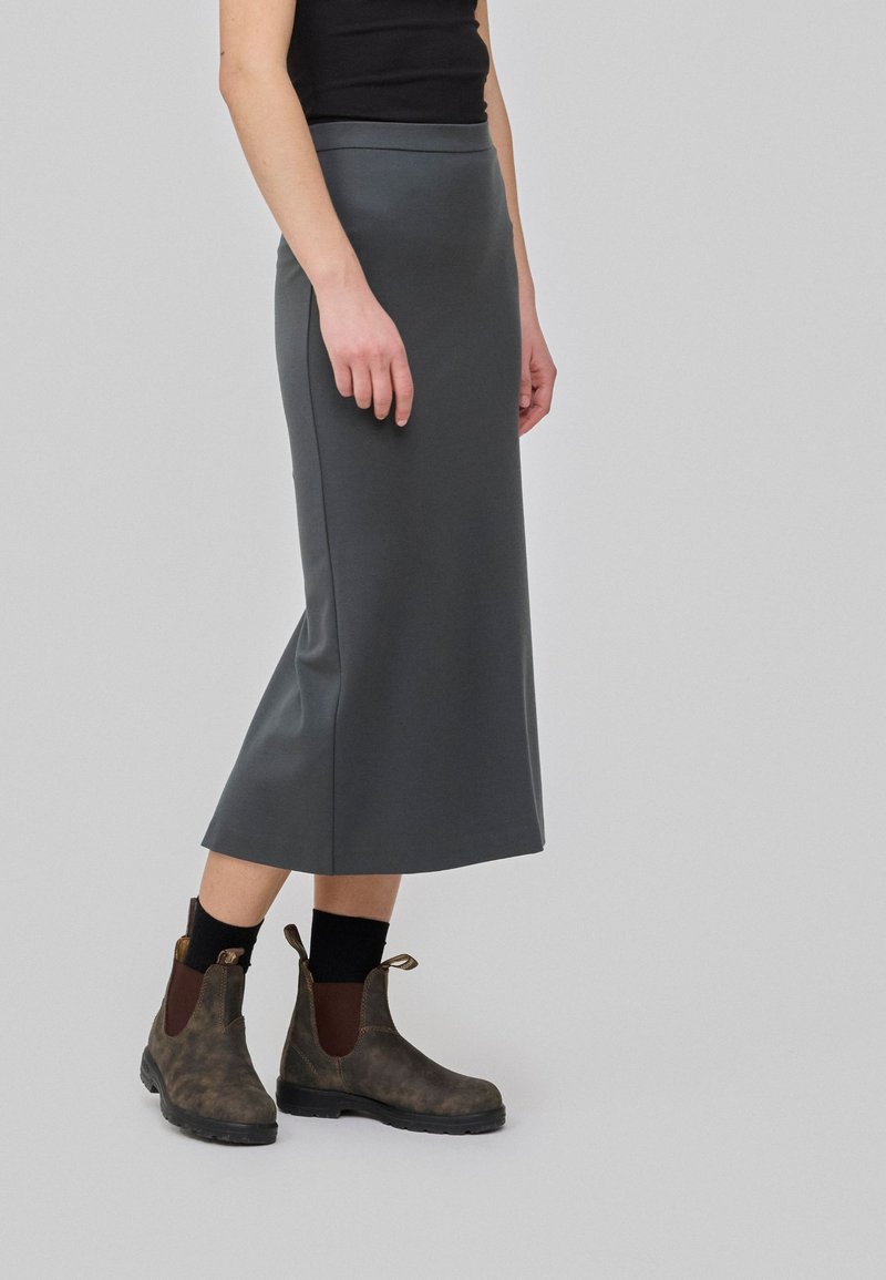 Jupe midi grise avec une taille élastique, assortie à des bottines brunes avec un panneau élastique sur le côté et une languette de tirage au talon.