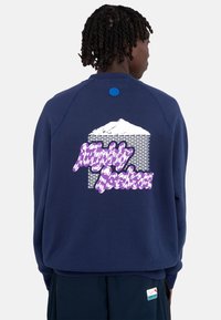 Sudadera de cuello redondo azul marino con un gráfico de montaña blanco y texto morado estilizado en la parte posterior. Tejido texturizado con un corte relajado.
