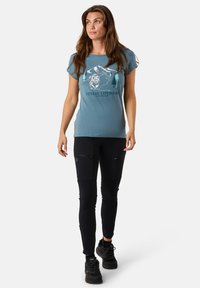 Light blue cotton t-shirt with outdoor graphic featuring mountains and a bear, paired with black stretchy pants, and black footwear.