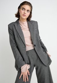 Grijze op maat gemaakte blazer met notched kleppen en een enkele knoopsluiting, gecombineerd met een lichtroze geribbelde top met geplooide manchetten.