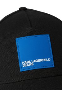 Fekete sapka texturált anyagból, kék téglalap alakú folttal, amelyen fehér szöveg olvasható: "KARL LAGERFELD JEANS."