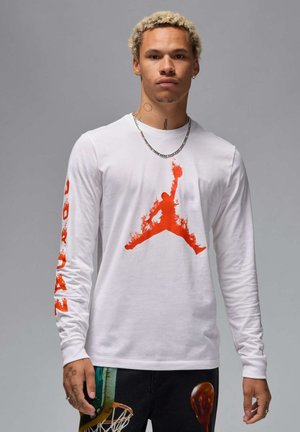 Long-sleeve white t-shirt featuring a large orange Jordan logo print on the front and orange text on the left sleeve. Cotton fabric.