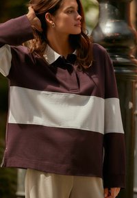 Lila und weiße Langarm-Polo-Sweatshirt mit Kragen und drei farblich abgesetzten Abschnitten, aus weichem, strukturiertem Stoff gefertigt.