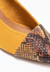 Ballerine in suede giallo con punta appuntita e cappuccio in materiale sintetico a fantasia multicolore. Sono visibili dettagli testurizzati.