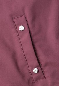Close-up of a burgundy fabric panel with two silver snap buttons and visible stitching along the edges.