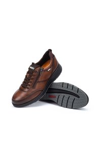 Zapatillas de cuero marrón con acabado suave, presentan un cierre frontal con cremallera y diseño con cordones, suela de goma con agarre texturizado para tracción.