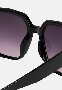 Czarne okulary przeciwsłoneczne o szerokim, kanciastym kształcie, z gradientowymi fioletowymi soczewkami i błyszczącymi oprawkami. Zawiasy są smukłe i płaskie.