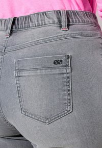 I jeans in denim grigio presentano una cintura contornata, una tasca posteriore con un design ricamato e dettagli di cucitura visibili.