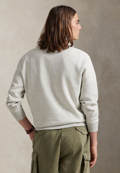 Sweatshirt cinzento claro com punhos e bainha canelados, apresentando um design clássico com decote redondo. Combinado com calças cargo verde oliva.