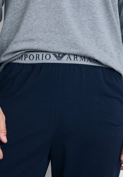 Tumesinised spordipüksid elastse pehmendusega, millel on hall Emporio Armani logo. Pehme kangas; lõdva istuvusega; kergelt nähtav tekstuur.