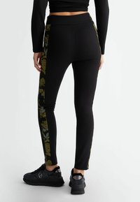 Leggings negros con acentos laterales de estampado floral, confeccionados en tejido elástico, presentan una cinturilla alta y un diseño ceñido.