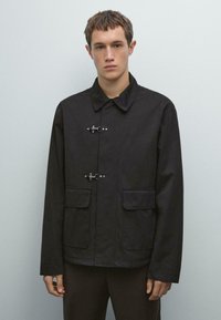 Black jacket featuring a button-up front with silver hardware, large patch pockets, and a classic collar. Smooth fabric with a slightly structured fit.
