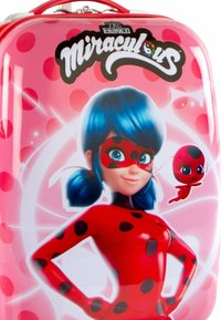 Valigia rigida rosa con un personaggio dai capelli blu e un costume a pois rossi, decorata con punti neri e una giocosa coccinella rossa.