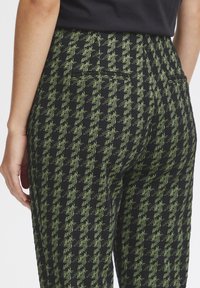 Pantalons noirs avec un motif pied-de-poule vert, tissu texturé, coupe slim, taille mi-haute et poches arrière.