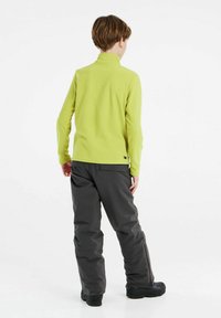 Maglione verde in felpa a maniche lunghe con colletto alto, abbinato a pantaloni grigio scuro. Il materiale sembra morbido, il tessuto è strutturato; design aderente.