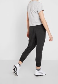 Graues, kurz geschnittenes T-Shirt mit kurzen Ärmeln, kombiniert mit dunkelgrauen Jogginghosen mit elastischen Bündchen und lockerem Schnitt, getragen mit weißen Turnschuhen.