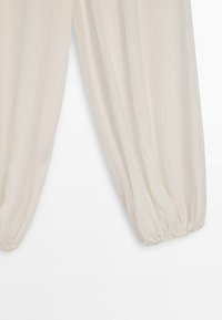 Lyse beige løse bukser med elastiske, rynkede ankler på en ensartet hvid baggrund.