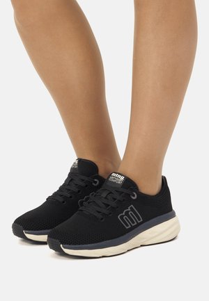 Zapatos deportivos negros hechos de material de malla, con cordones, una suela de color claro y un logo sutil en el lateral.