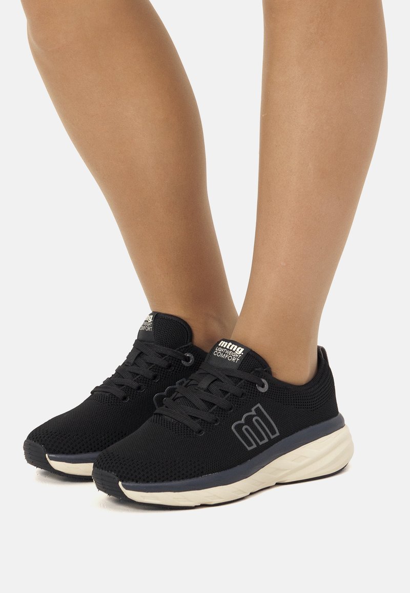 Zapatos deportivos negros hechos de material de malla, con cordones, una suela de color claro y un logo sutil en el lateral.