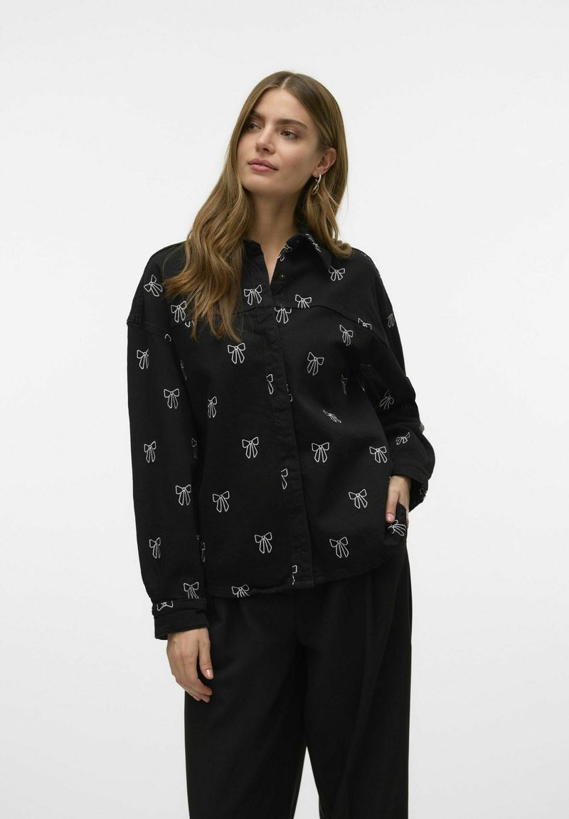 Zwarte shirt met witte strikpatronen, gemaakt van een zachte stof, met een kraag en lange mouwen, sluiting met knopen aan de voorkant en zakken.