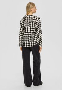 Zwart-wit houndstooth patroon blouse met lange mouwen, ronde halslijn en licht gerimpelde manchetten, gecombineerd met hoge taille zwarte broeken.