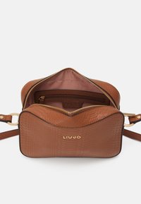 Borsa a tracolla in pelle marrone con texture, acciaio dorato e logo. Presenta una chiusura con cerniera e un ampio scomparto interno.