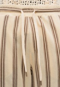 Shorts en lin avec un motif à rayures beige et marron, dotés d'une taille à cordon de serrage et d'accents métalliques aux extrémités du cordon.