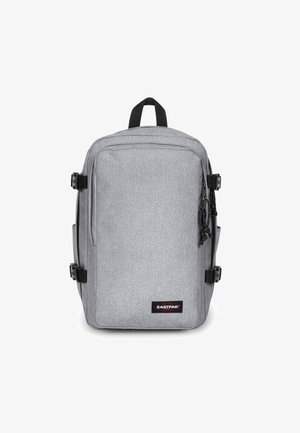 Šedý látkový batoh se strukturovaným designem, který má přední zipy, boční kapsy a černé nastavitelné popruhy. Zobrazeno logo Eastpak.